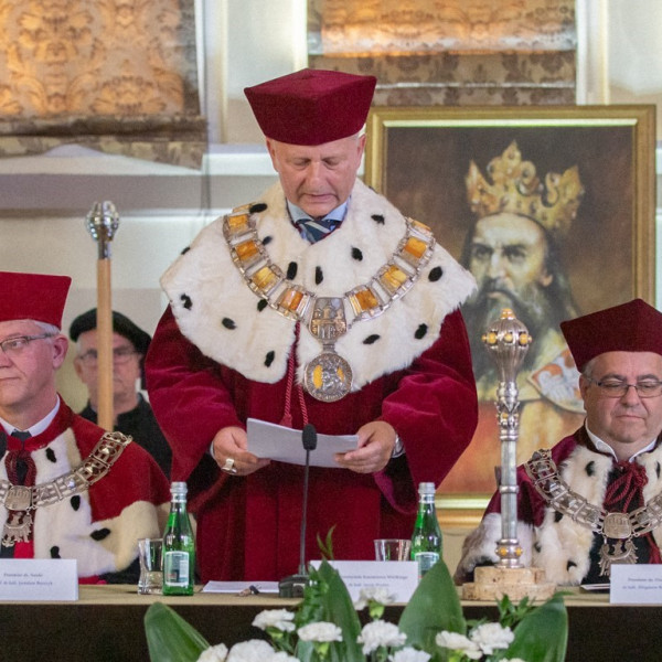 Kolegium retorskie, panowie ubrani w togi rektorskie siedzą przy stole prezydialnym, rektor stoi i przemawia
